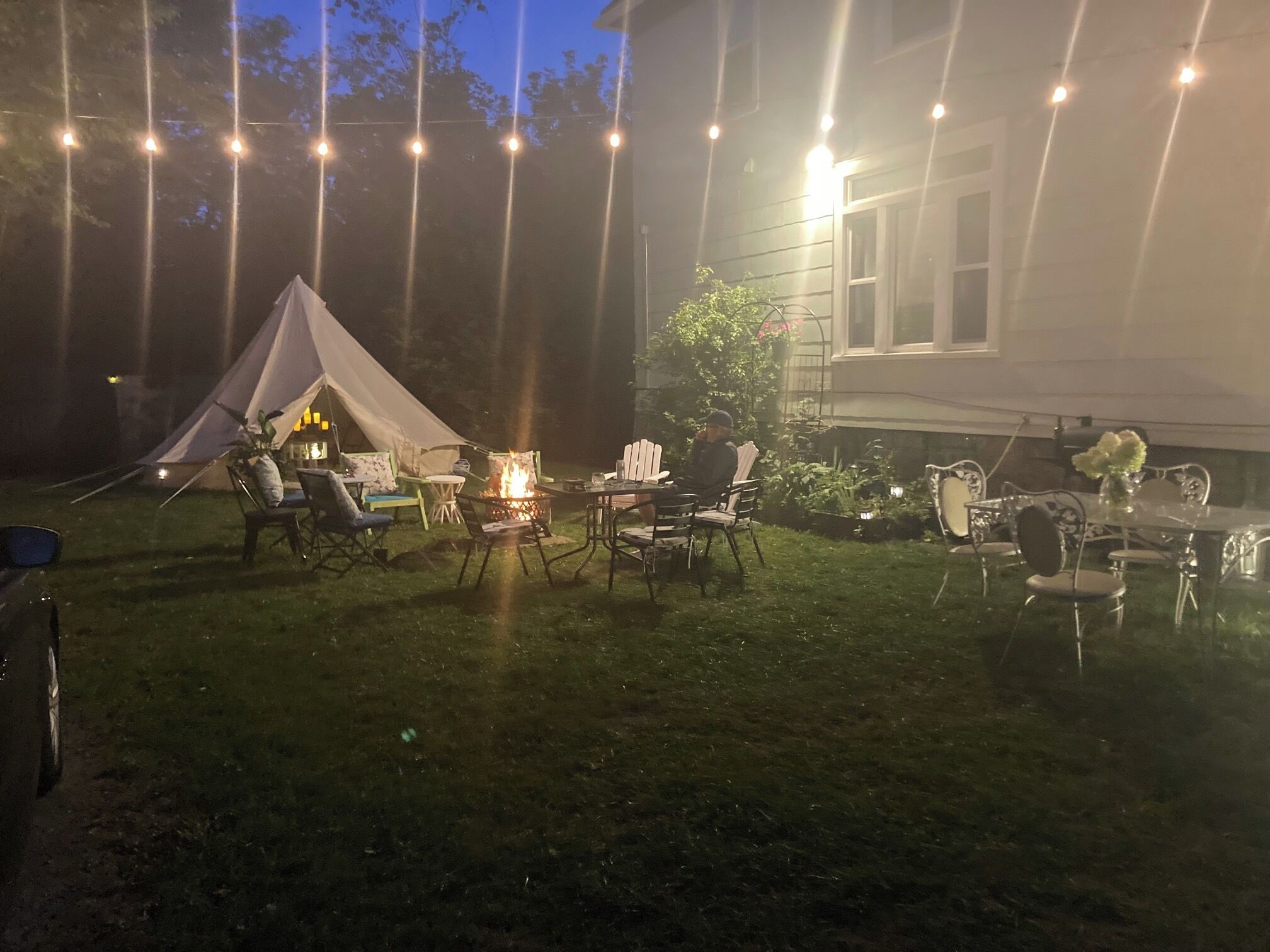 Uma área de pátio ao ar livre com uma tenda, um braseiro e uma mesa de jantar montada para um evento noturno.
