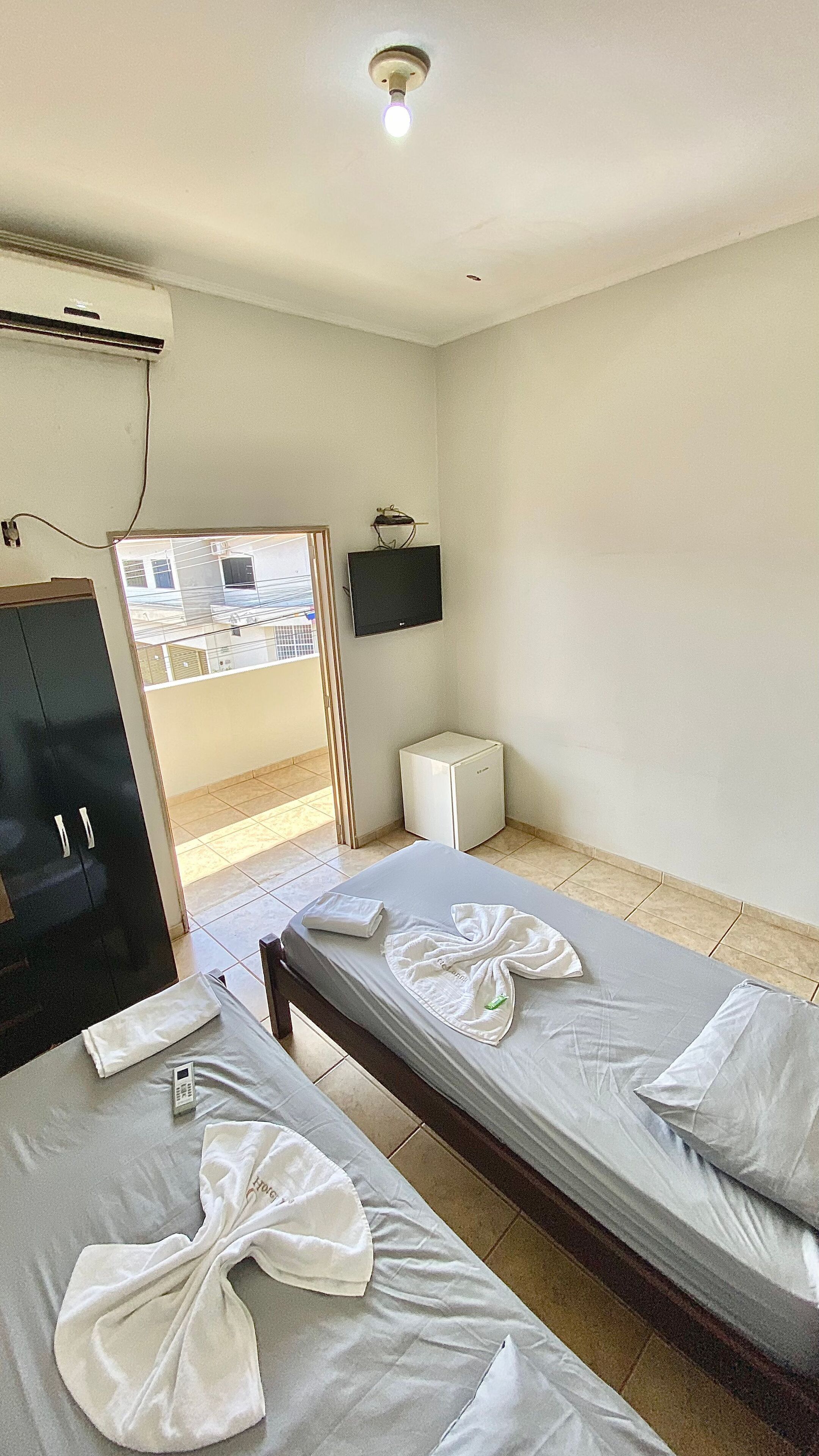 A hotel room with two single beds, a small white cabinet, a television on the wall, and an air conditioning unit.