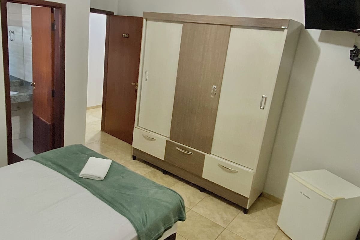 Habitació d'hotel amb llit, escriptori, armari, televisió i nevera petita.