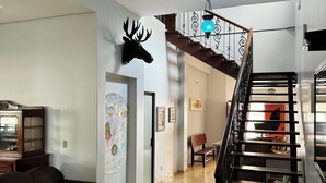 A spacious living area with a brown sofa, a mounted deer head, a staircase with a metal railing, and a decorative ceiling light. - Hotel Lunna (Porto Nacional)