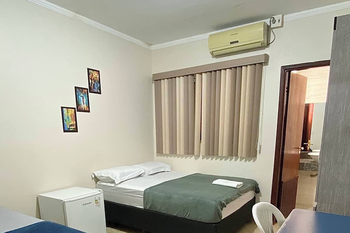 Habitació d'hotel amb dos llits, una taula petita, aire condicionat i una finestra amb cortines.
