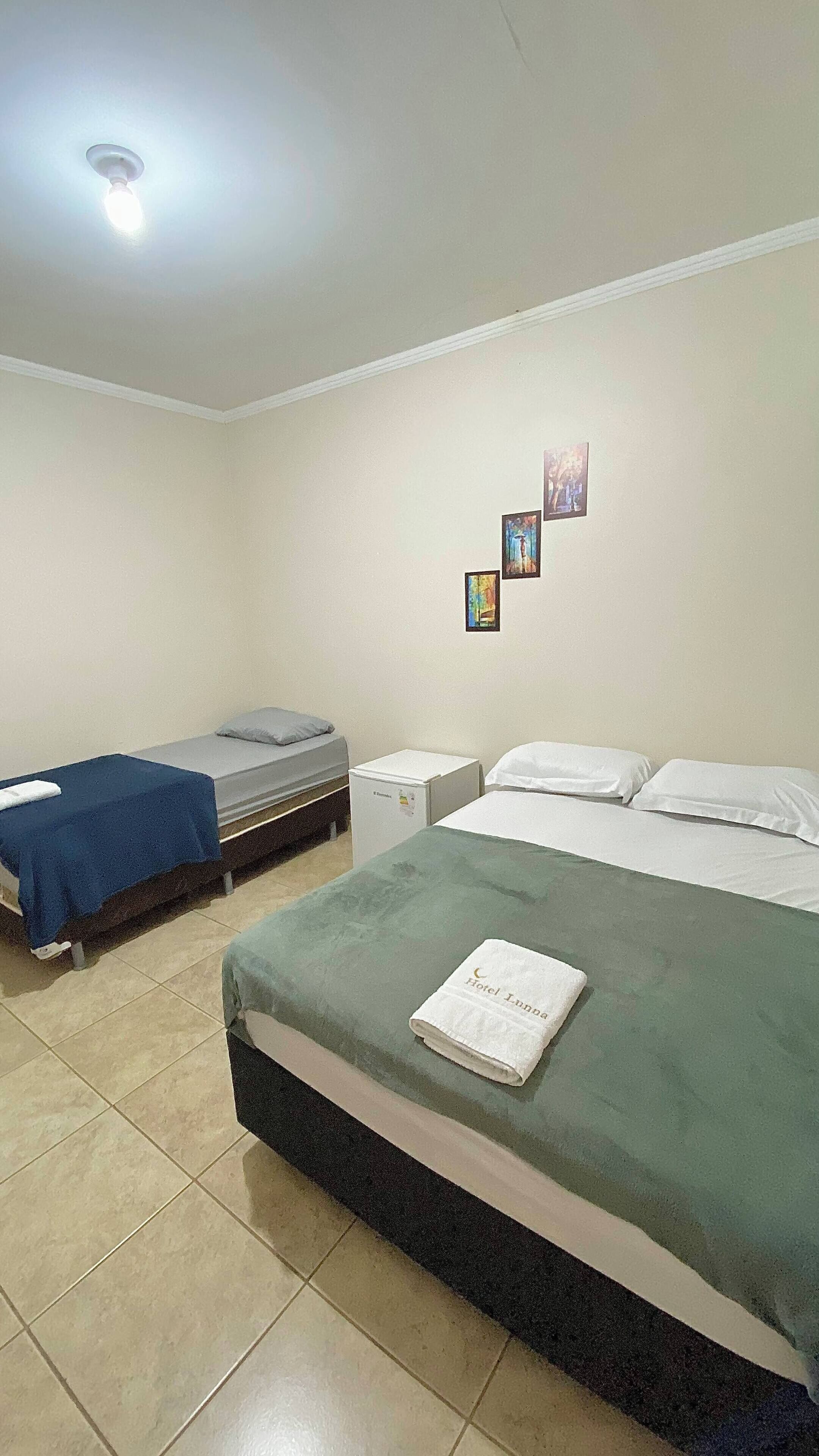 A hotel room with a large bed, two smaller beds, a refrigerator, and a ceiling light.