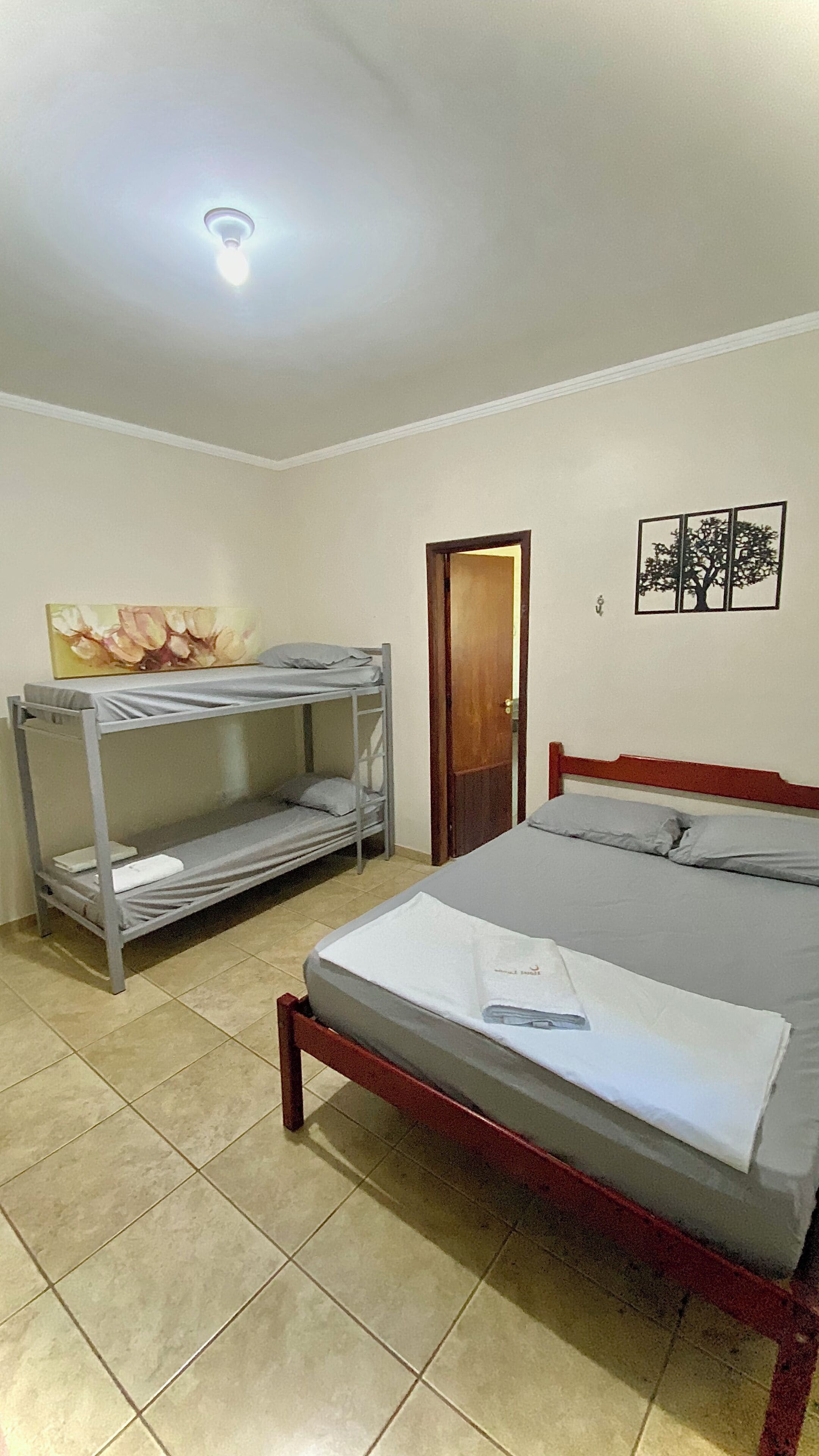 A room with a bunk bed, a single bed, a door, and a wall with a tree decoration.