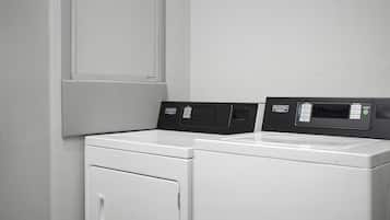Un área de lavandería con dos lavadoras blancas de carga frontal y un panel de control con varias opciones.