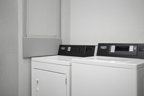 Un área de lavandería con dos lavadoras blancas de carga frontal y un panel de control con varias opciones.