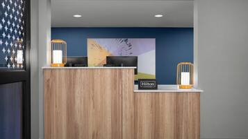 Una recepción de hotel con detalles de madera, una pared de acento azul y dos apliques iluminados.
