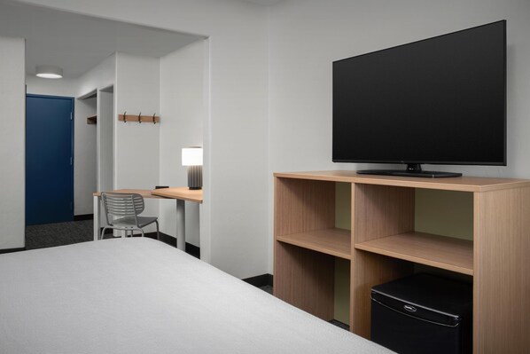 Habitación de hotel con cama, escritorio con silla, televisor sobre un mueble bajo y armario.