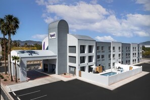 Een modern hotel met een zwembad, een overdekte ingang en een berg op de achtergrond.