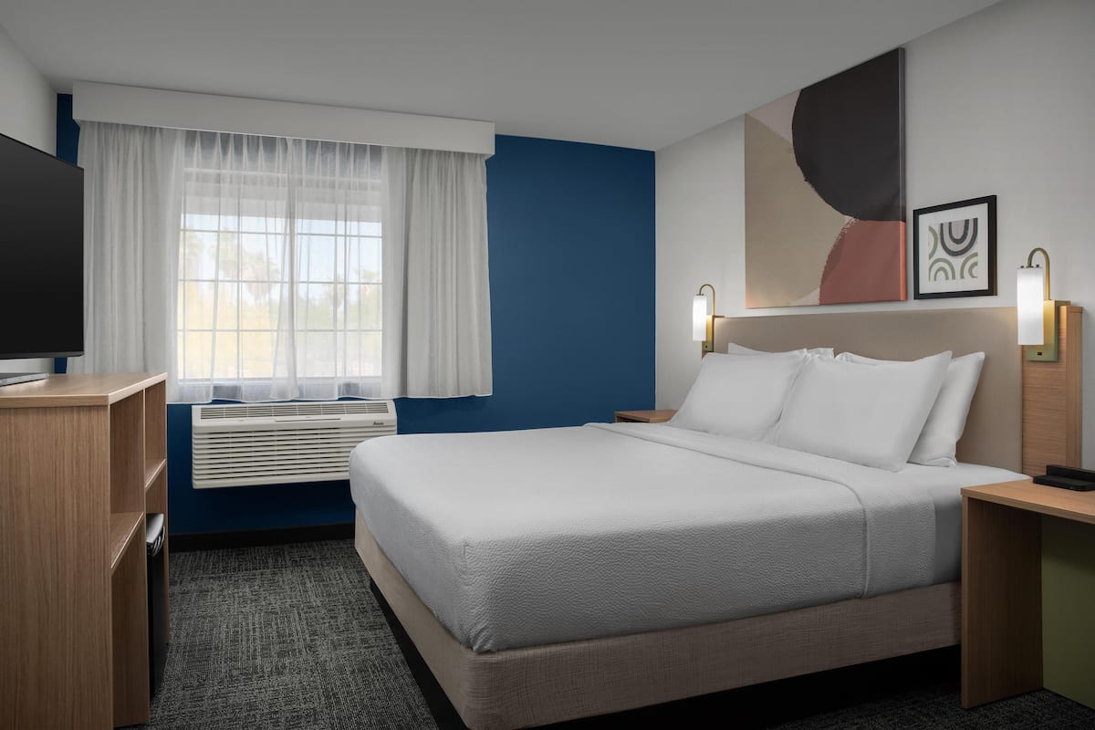 Hotelkamer met een bed, bureau, televisie, raam met gordijnen en kunst aan de muur.