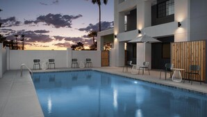 Une piscine avec des chaises et des tables, une clôture en bois et une vue sur le coucher de soleil.