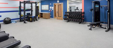 Ein Fitnessstudio mit Laufbändern, Kraftgeräten und einem Wand-Squat-Rack.
