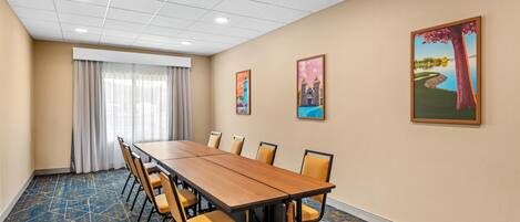 A conference room with a long table, chairs, and a large window with curtains.