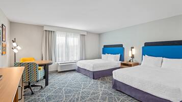 A hotel room with two beds, a desk, a chair, and a window with curtains.