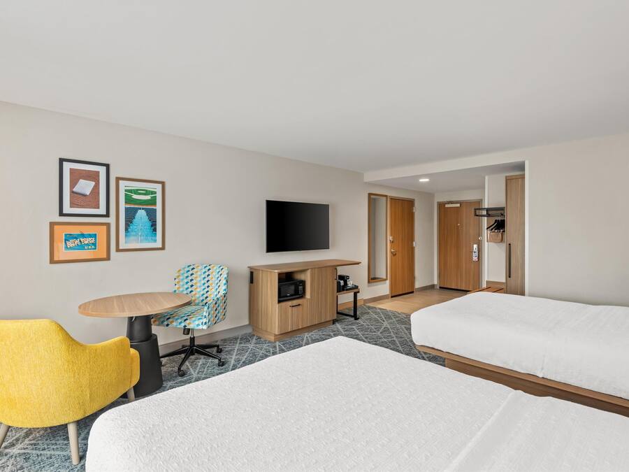 Quarto de hotel com duas camas, televisão, secretária pequena e uma cadeira.