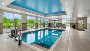 An indoor swimming pool with a view of greenery outside, large windows, and a blue ceiling. - Hampton Inn Cooperstown (Cooperstown)