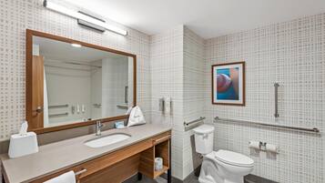 A modern bathroom with a wooden vanity, a large mirror, a toilet, and a handrail.