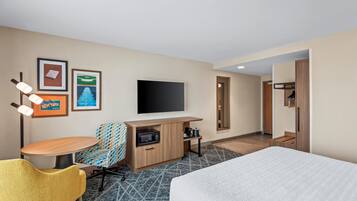 Ein Hotelzimmer mit einem Bett, einem Schreibtisch, einem Flachbildfernseher, einer Mikrowelle, einem Sessel und einem kleinen Tisch.