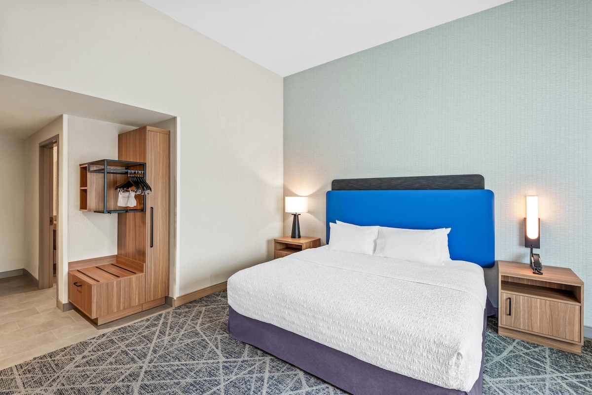 A hotel room with a bed, wooden wardrobe, two bedside tables with lamps, and a patterned carpet.