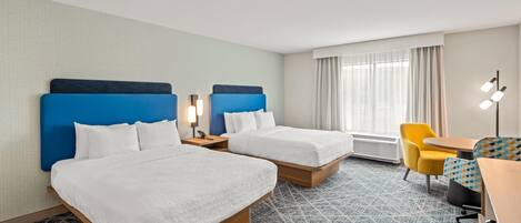 A hotel room with two beds, a desk, a chair, and a lamp.