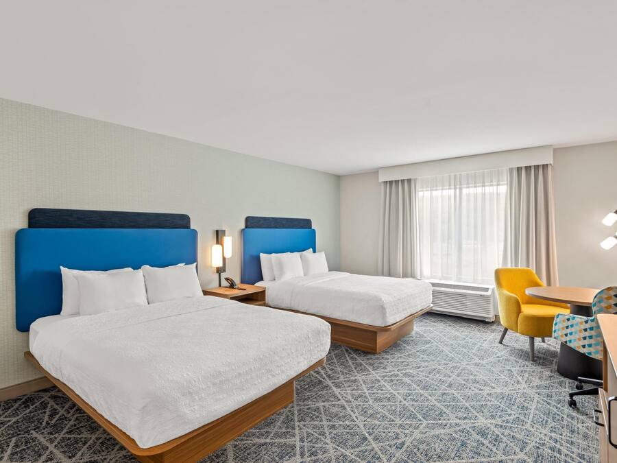 Una habitación de hotel con dos camas, un escritorio, una silla y una lámpara.