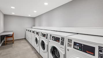 A laundry room with multiple commercial washers and dryers, a small desk with a chair, and a tiled floor.