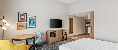 Ett hotellrum med en säng, ett skrivbord med en stol, en tv och en garderob.