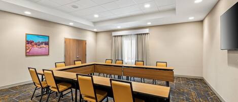 A conference room with a long table, chairs, a door, a window with curtains, and a television on the wall.