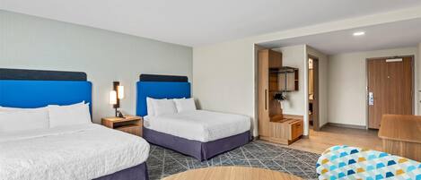 A hotel room with two beds, a wooden desk, a chair, and a wardrobe.