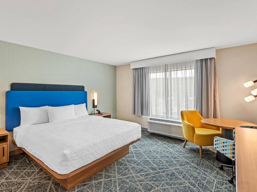 A hotel room with a large bed, a desk, a chair, and a window with curtains.