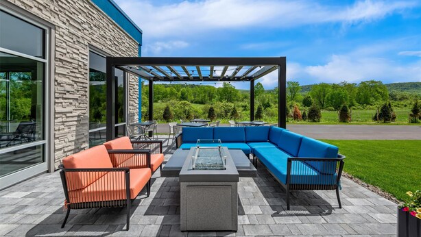 An outdoor patio with a stone wall, a blue sofa, orange chairs, and a glass-top table. - Hampton Inn Cooperstown (Cooperstown)