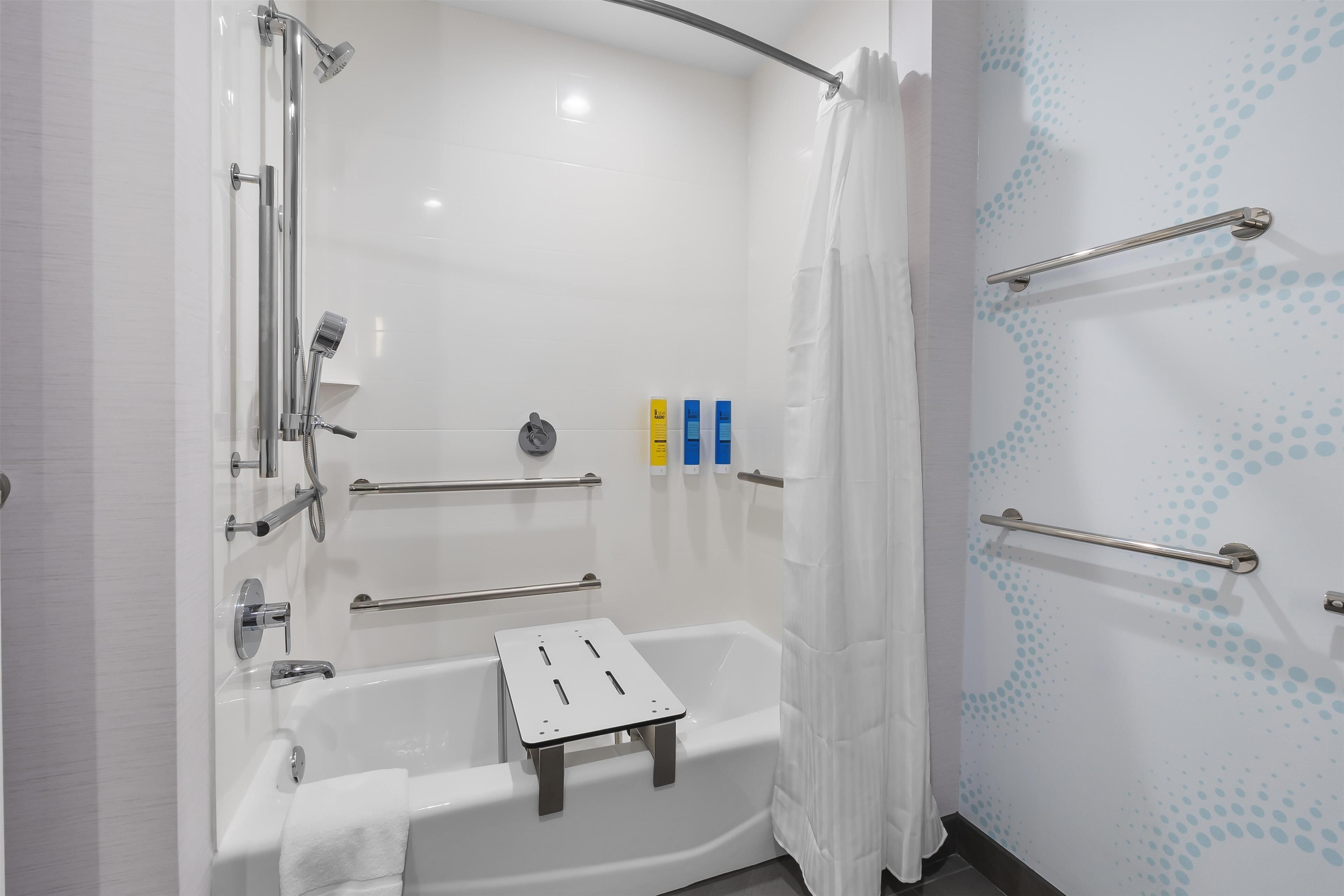 A modern bathroom with a bathtub, shower, and handrails.