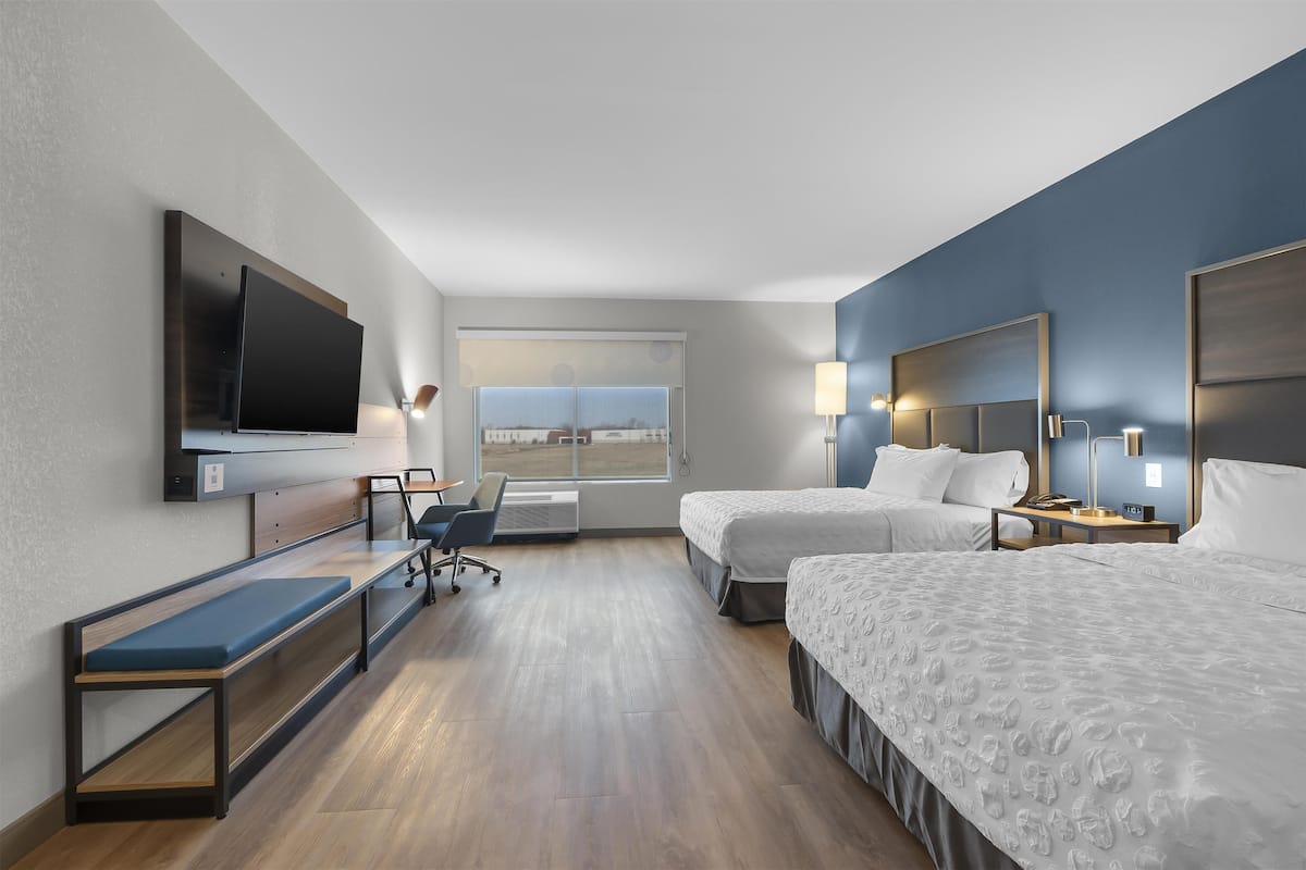 Een hotelkamer met twee bedden, een bureau, een stoel, een televisie en een raam met uitzicht.