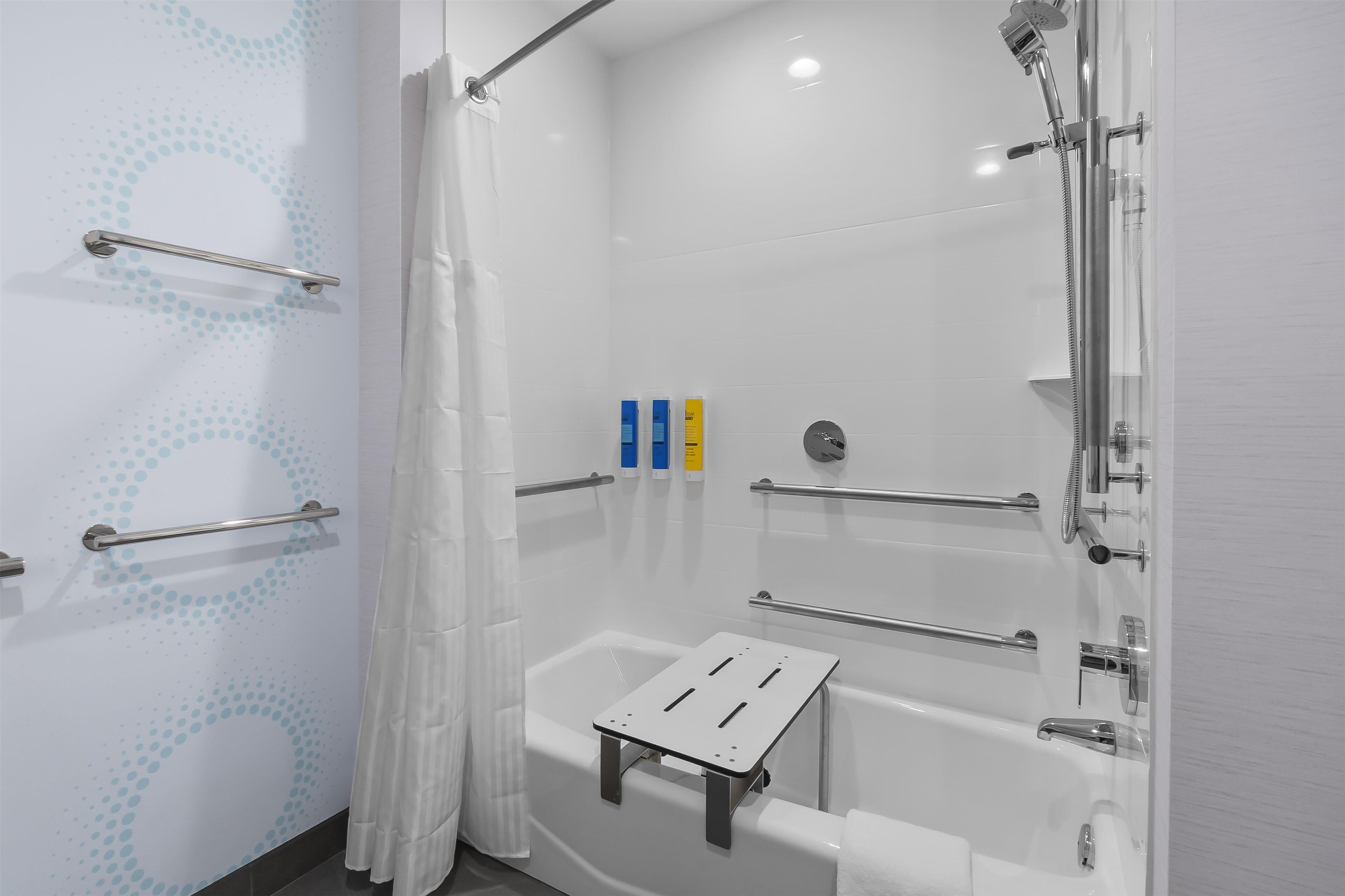 A modern bathroom with a walk-in shower, grab bars, and a white bathtub.