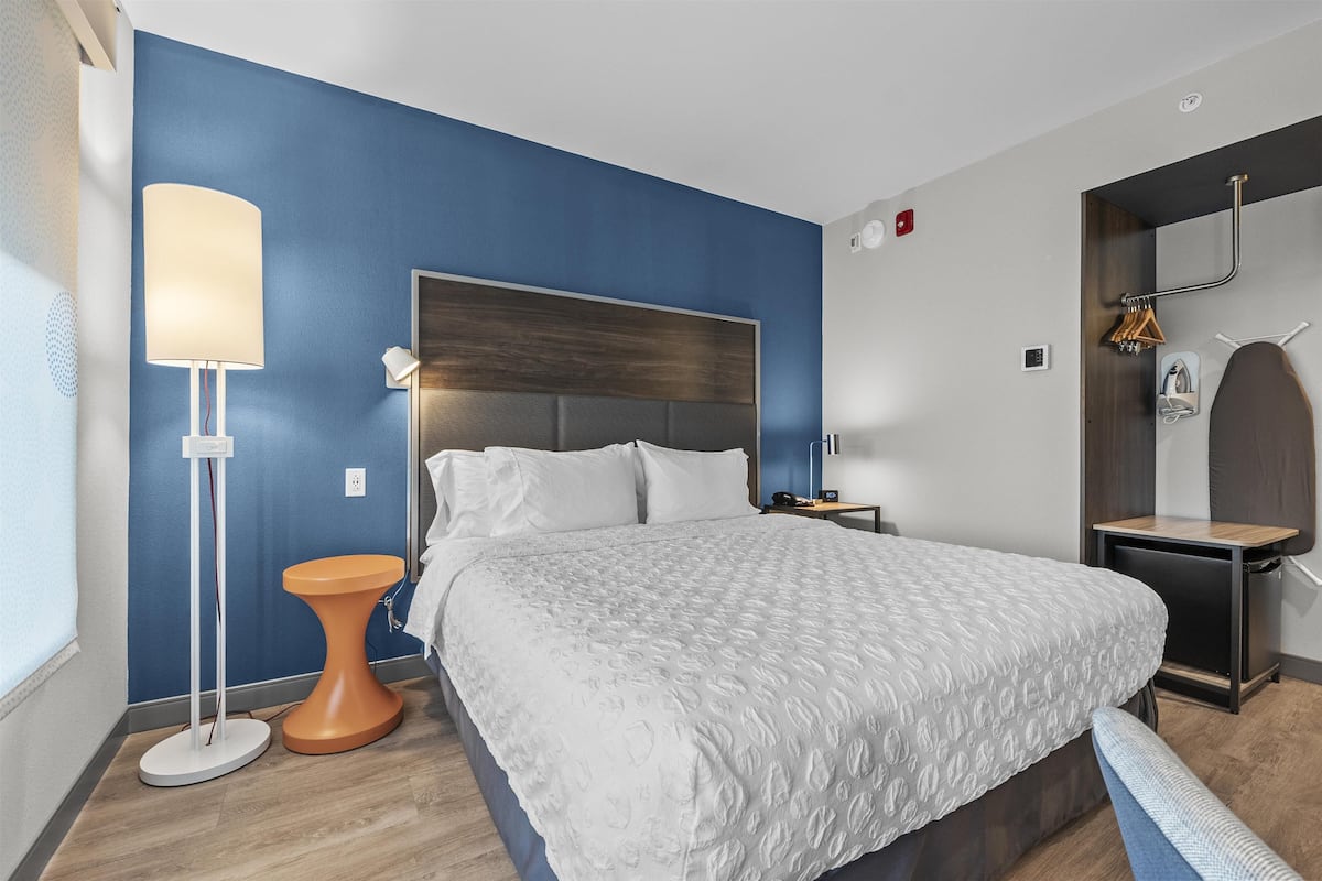 Een moderne hotelkamer met een groot bed, nachtkastje, lamp en een kledingkast.