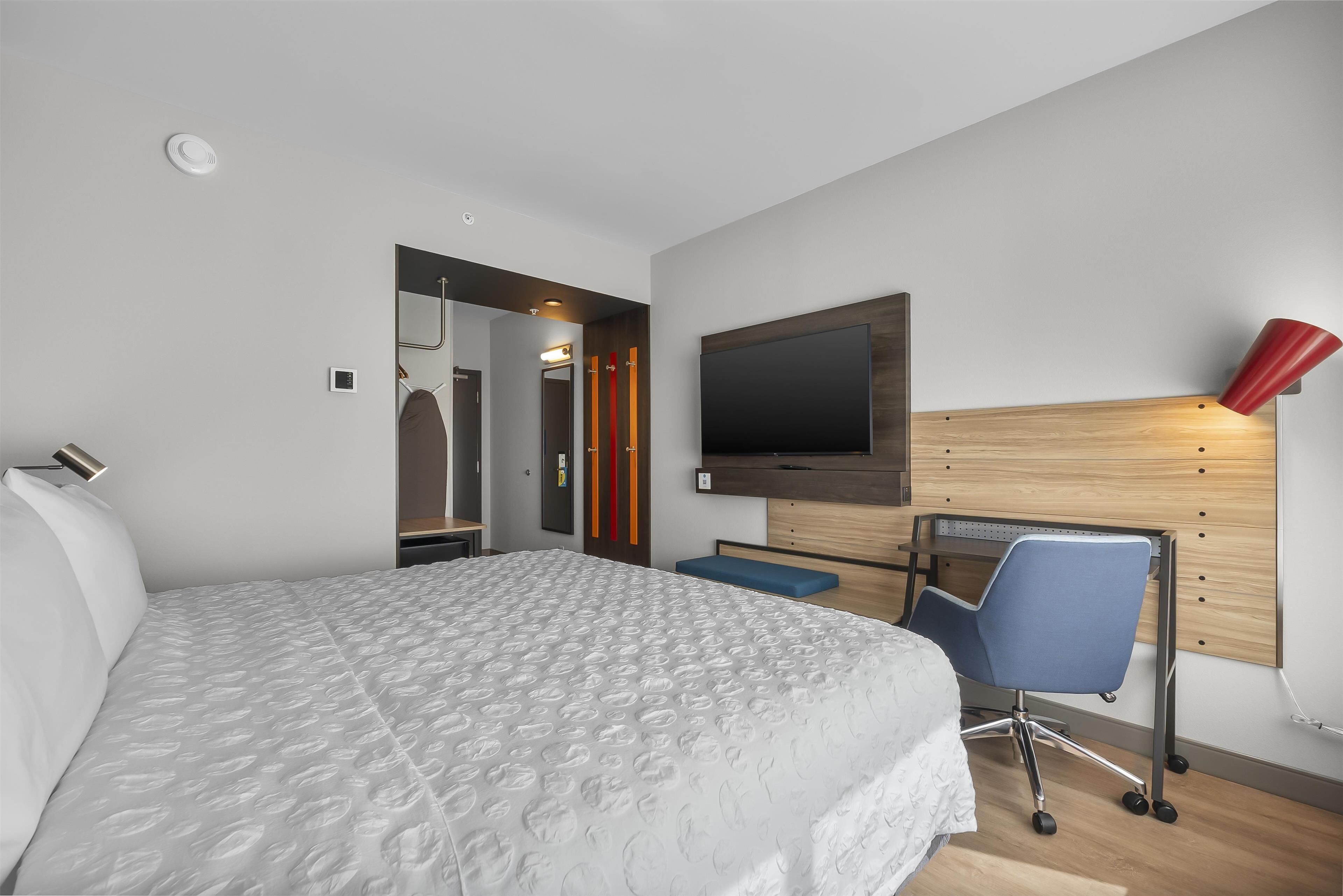 A modern hotel room with a large bed, a desk with a chair, a flat-screen TV, and a red lamp.
