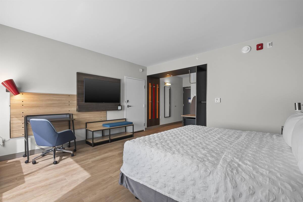 Een moderne hotelkamer met een groot bed, een bureau met stoel, een aan de muur bevestigde televisie en een deur naar de badkamer.