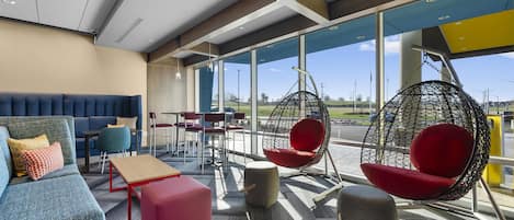 Un moderno espacio lounge con opciones de asientos, incluyendo sofás, sillones y una silla colgante, con ventanas amplias que ofrecen vistas al exterior.
