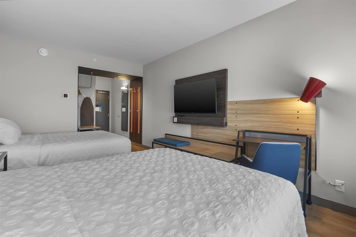 Een hotelkamer met twee bedden, een televisie, een rode lamp en een houten hoofdeinde.