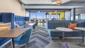 A modern indoor seating area with blue sofas and tables, a patterned carpet, and large windows offering a view of the outdoors. - Tru By Hilton Cape Girardeau (Cape Girardeau)