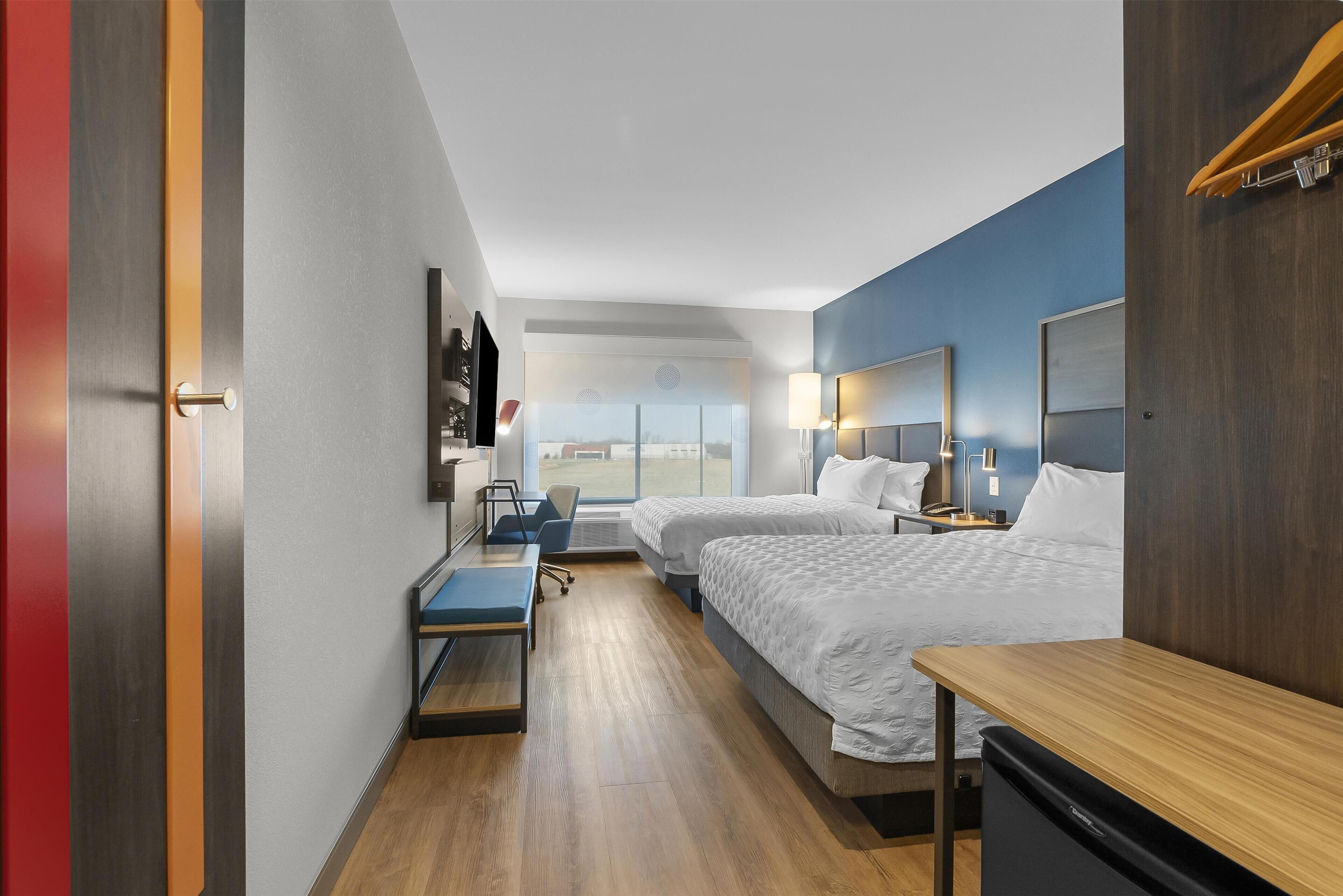 A modern hotel room with two beds, a desk, a chair, and a small table.
