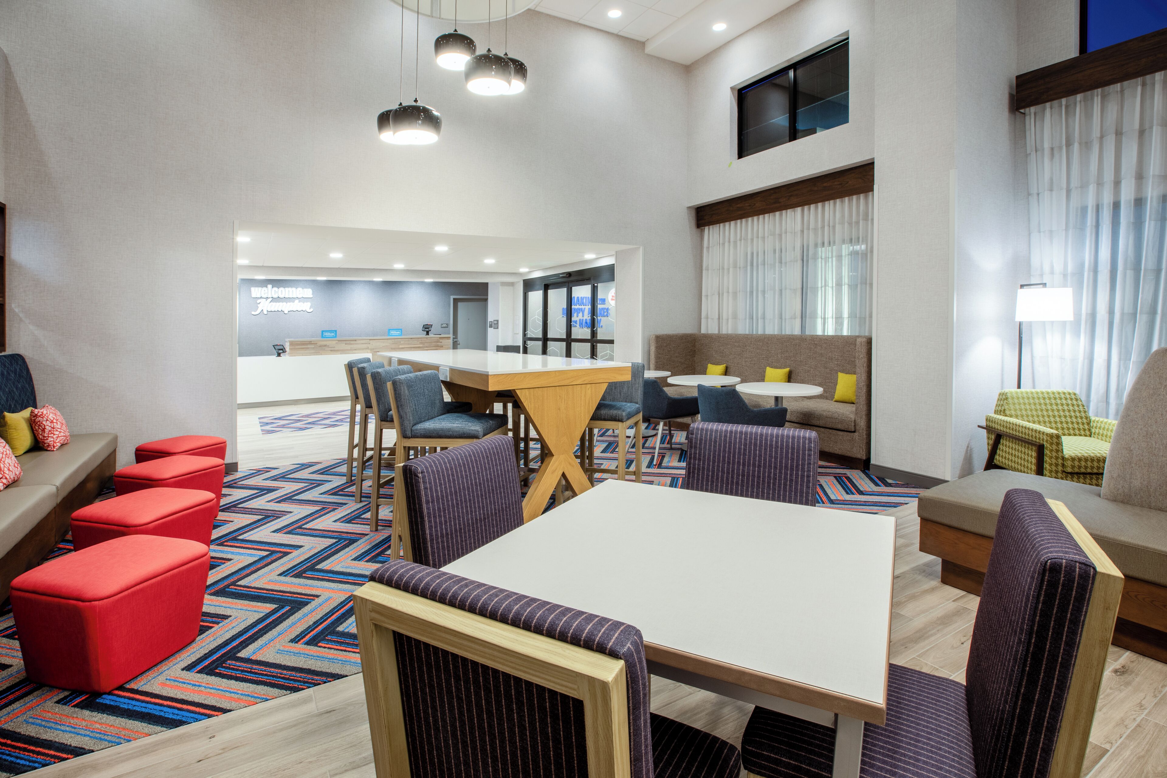 A modern hotel lobby with a central dining area, seating arrangements, and a reception desk.