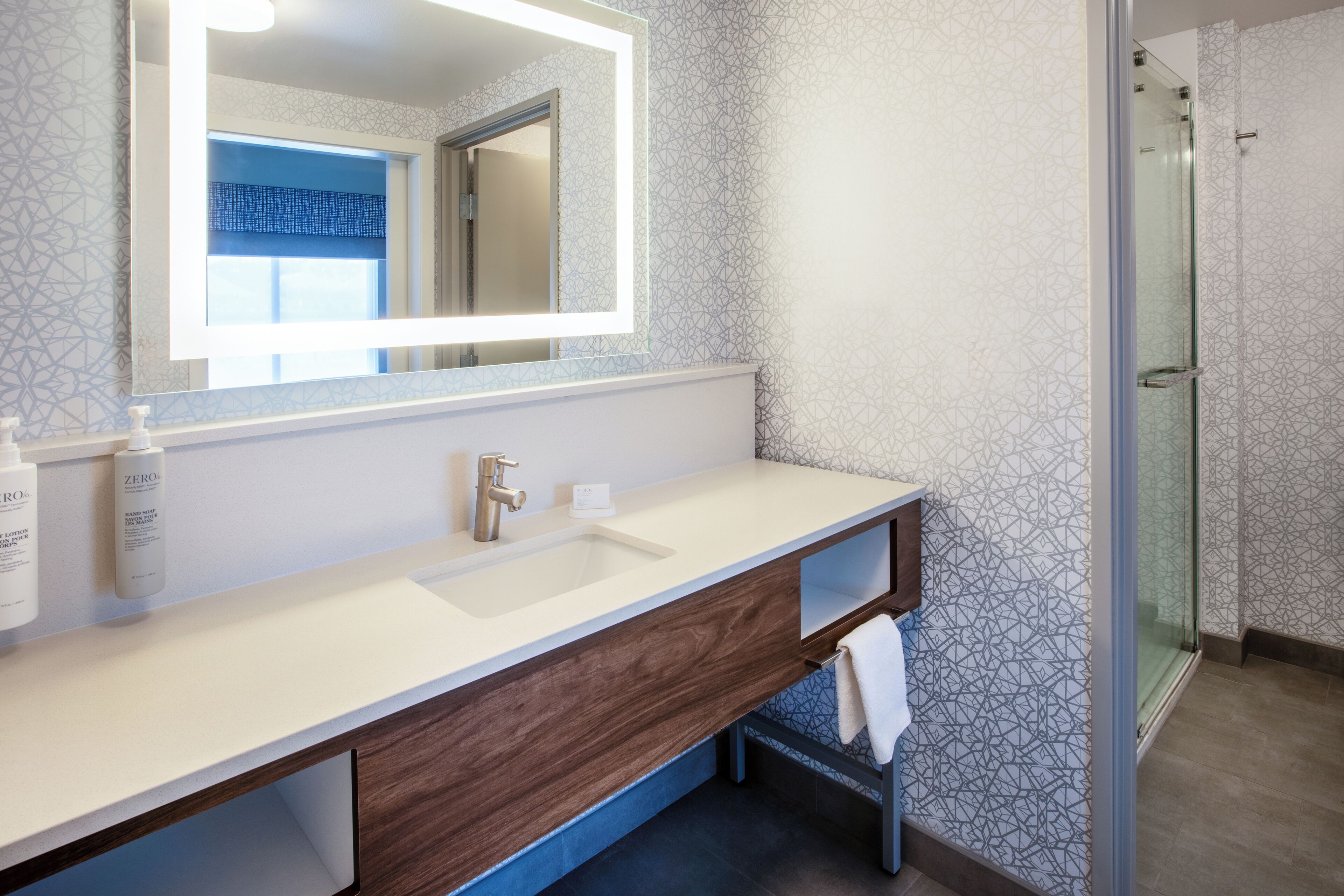 Une salle de bain moderne avec un grand miroir, un lavabo blanc, un meuble-lavabo en bois et une cabine de douche en verre.