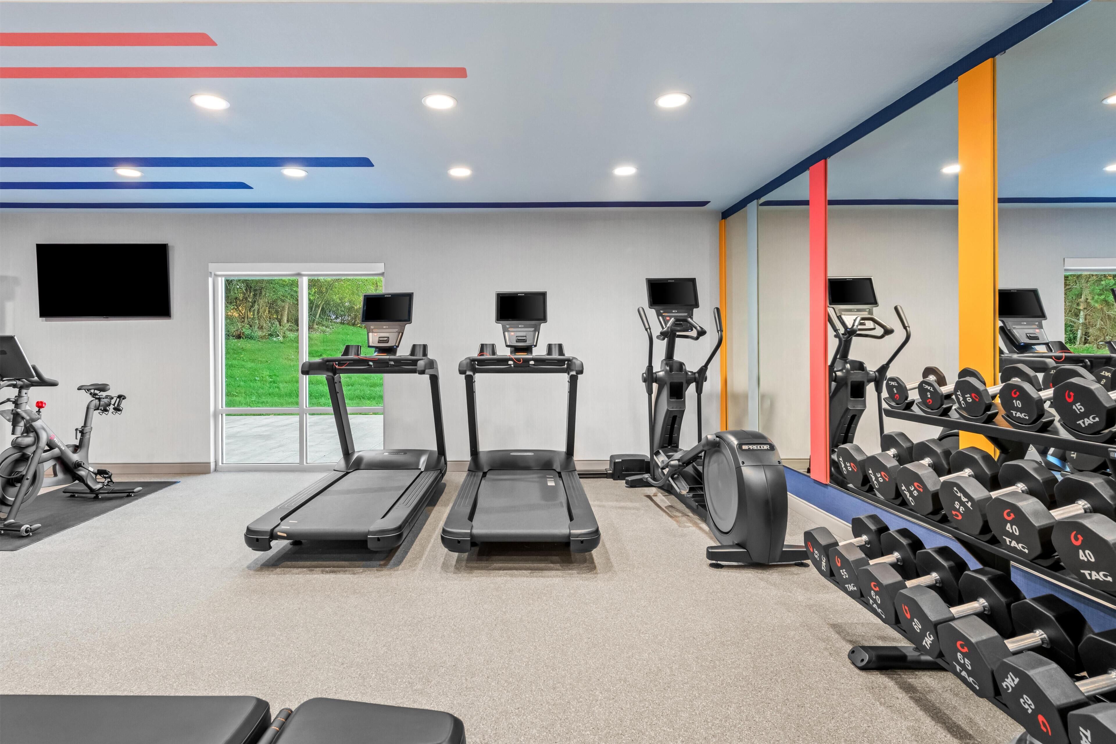 Une salle de sport équipée de tapis de course, de vélos elliptiques et d’un porte-haltères.