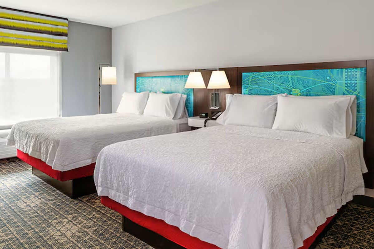 Une chambre d’hôtel avec deux lits, une table de chevet, une lampe et une fenêtre donnant sur un beau paysage.