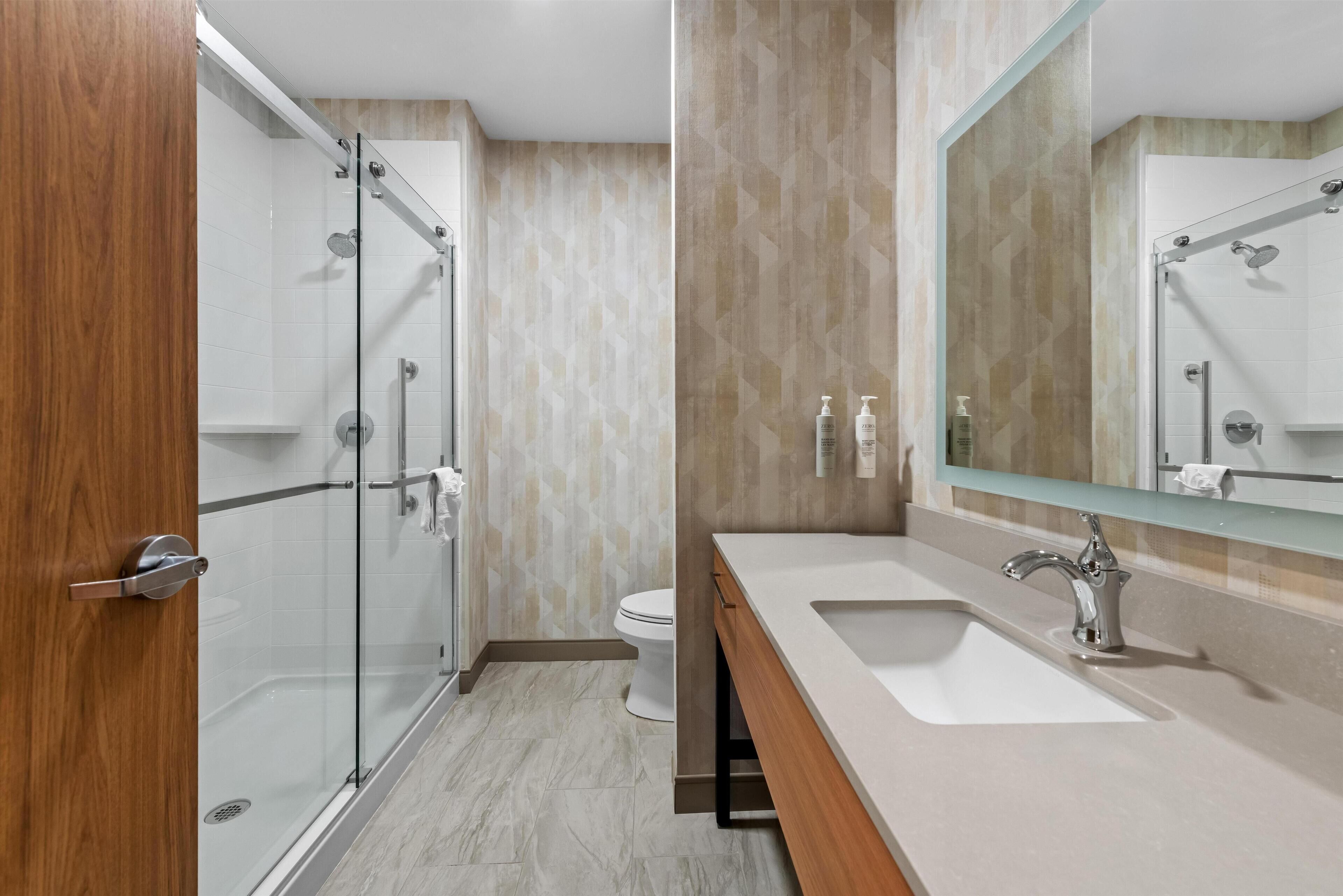 Une salle de bain moderne avec une douche à parois de verre, un lavabo blanc avec un grand miroir et des toilettes.