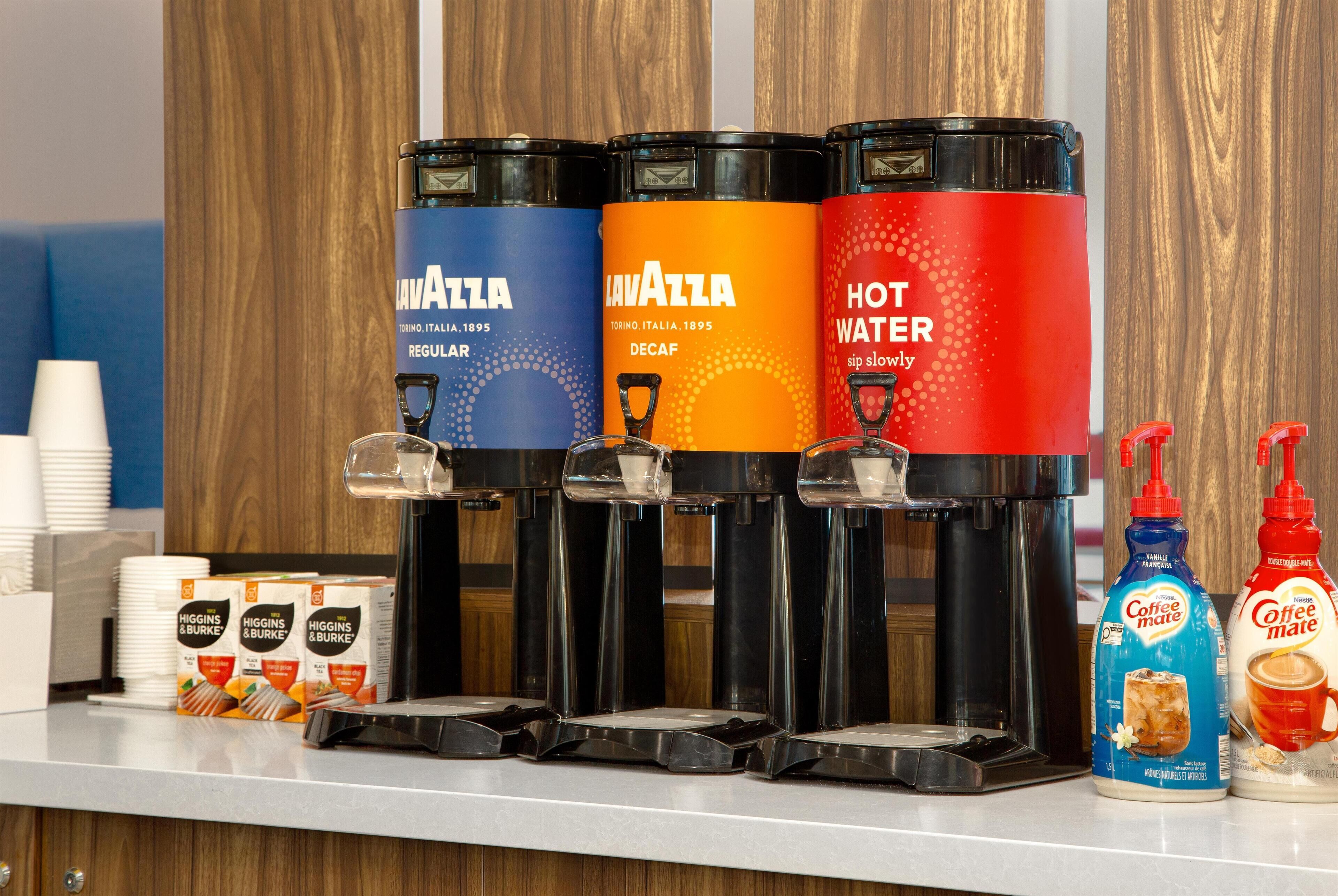 A coffee station with three dispensers labeled 'Lavazza' and 'Hot Water', and two bottles of 'Coffee Mate'.