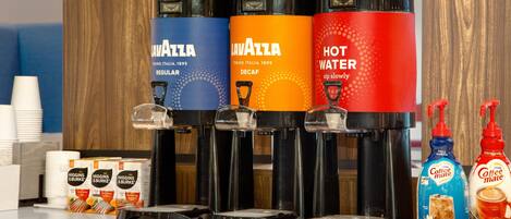 A coffee station with three dispensers labeled 'Lavazza' and 'Hot Water', and two bottles of 'Coffee Mate'.