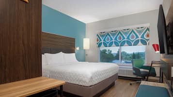 A hotel room with a bed, a desk, a chair, a TV, and a window with a view of the outside.