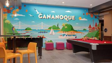 A pool table and chairs in a room with a mural of Gananoque, a bridge, and boats.