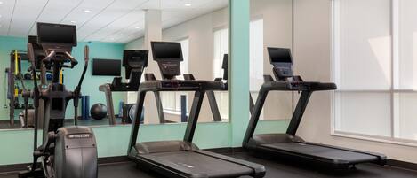 Un gimnasio con cintas de correr, elíptica y bicicleta estática, con un espejo grande y ventanas.